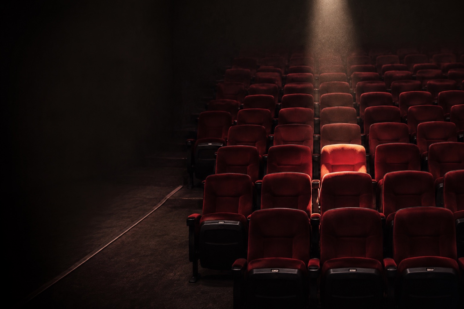 Rows of red cinema seats with one lit by a spotlight